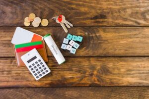 Flat lay of a calculator, colorful wallets, coins, keys, and math cubes on a wooden table, suggesting financial organization.