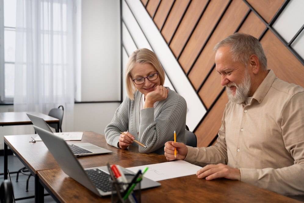 Two people engaged in a discussion at a wooden table, surrounded by a laptop, papers, and stationery, in a modern office setting.