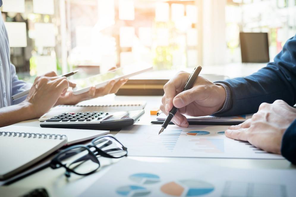 Two professionals analyze financial charts and data on a conference table, using a tablet and calculator for collaboration.