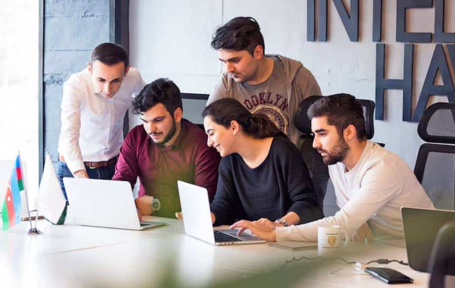 A group of professionals collaborates around laptops in a modern office.