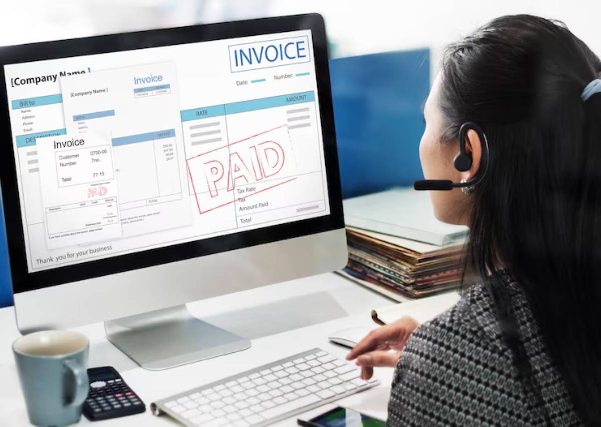 A woman wearing a headset reviews invoices on a computer screen, with