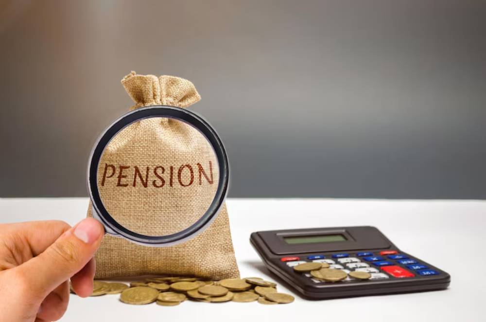 A hand holding a magnifying glass over a burlap sack labeled 'PENSION,' with a calculator and stacked coins nearby.